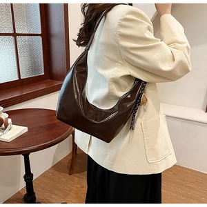 Detail of dark brown glossy crescent bag with small bear charm on model's shoulder