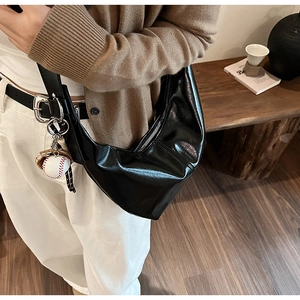Close-up of black glossy half-moon dumpling bag with creative baseball charm detail