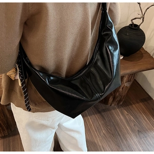 Black glossy crescent hobo bag styled on shoulder with a woven decorative charm
