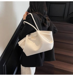 Close-up of white lychee leather texture and gold hardware on oversized shoulder bag