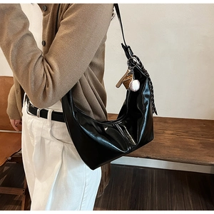 Detail showing the glossy finish and modern crescent shape of the black shoulder bag