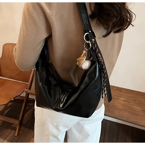 Detail of a black crescent hobo bag with baseball charm pendant worn by a model
