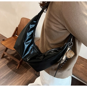Detail of a shiny black hobo bag with a cute bear charm, styled on a shoulder