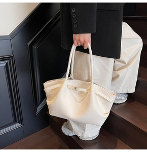 Detail of a large cream tote bag showing pebble leather texture and metal buckle