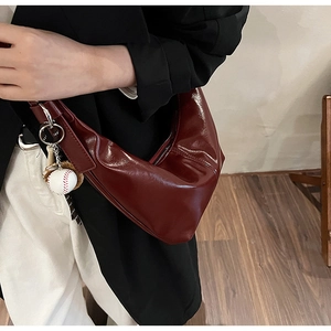 Detail of burgundy glossy leather hobo bag with baseball keychain and smooth texture
