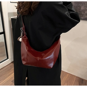 Close-up of deep red crescent shoulder bag with baseball charm on a black coat