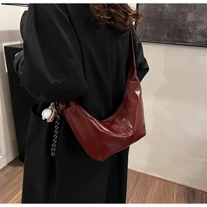 Deep burgundy glossy crescent bag detail with unique baseball charm on the zipper