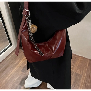 Detail of dark red hobo bag with glossy finish and owl charm on adjustable strap