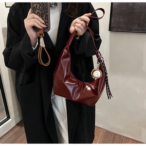 Detail of dark red patent leather hobo bag with baseball charm and striped ribbon