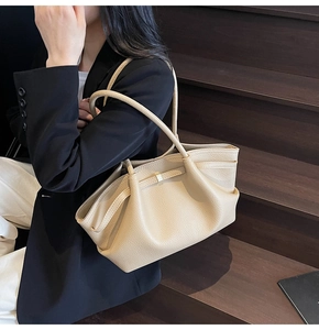Detail of beige textured leather tote featuring elegant side pleats and gold buckle hardware