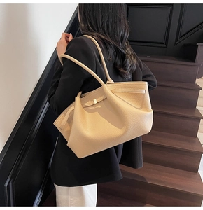 Close-up of beige lychee grain leather tote bag featuring a gold metal buckle detail