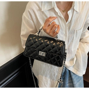 Détail d'un petit sac carré noir matelassé avec fermoir rotatif et chaîne argentée