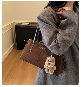 Détail du sac à épaule en daim marron foncé avec charme d'ours et plaque en métal