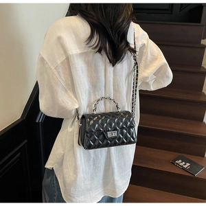Détail du sac matelassé noir avec fermoir rotatif argenté sur chemise en lin blanc