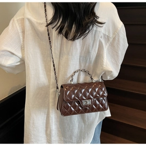 Détail d'un sac marron matelassé avec fermoir rotatif argenté et bandoulière chaîne