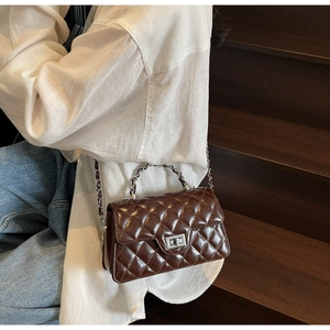 Sac bandoulière marron foncé matelassé avec chaîne en argent porté par un mannequin