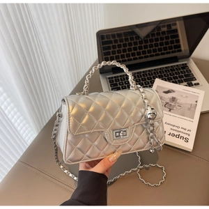 Détail d'un sac argenté matelassé avec chaîne métallique et poignée à bille sur bureau