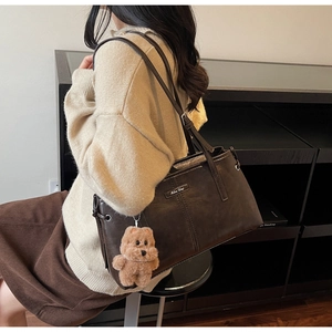 Détail d'un sac cabas marron foncé avec breloque ours porté sur un pull beige