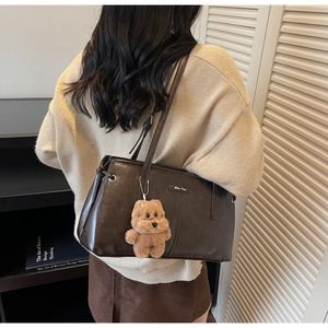 Détail du sac cabas en cuir marron foncé avec plaque en métal et breloque ours en peluche