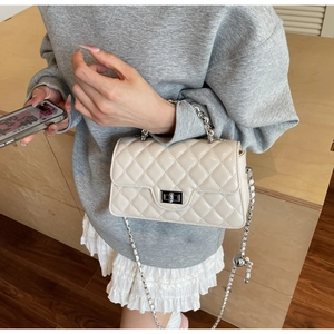 Détail du sac matelassé beige avec chaîne argentée et pendentif boule décoratif