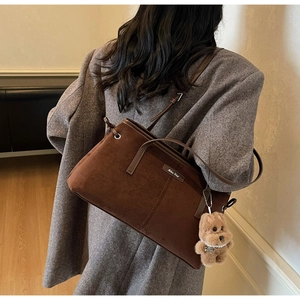 Détail d'un sac à main marron en daim avec logo en métal et pendentif ours en peluche