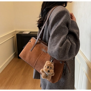 Détail du sac cabas en daim marron avec charm chiot en peluche et plaque de marque