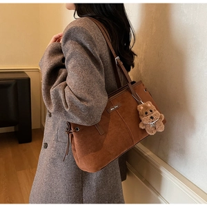 Détail du sac cabas en daim marron avec cordon à franges et breloque chiot sur blazer