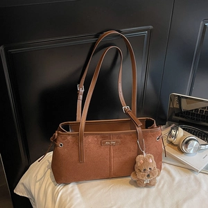 Détail du sac à bandoulière en daim marron avec plaque en métal et breloque ours