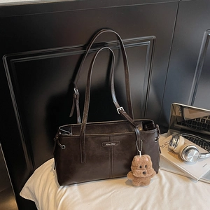 Détail d'un sac à bandoulière en cuir marron foncé avec logo métallique et pendentif ours