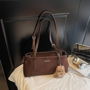 Détail d'un sac à main en daim marron avec pendentif ours à côté d'un livre d'art