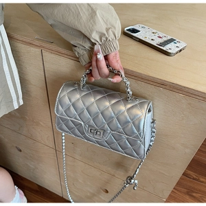 Détail du sac argenté matelassé avec poignée en chaîne métallique et fermoir rotatif