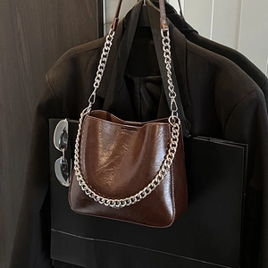 Brown oil wax leather bucket bag with silver chain strap on a black blazer