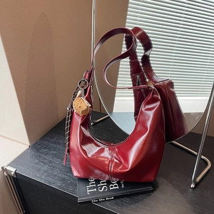 Retro burgundy dumpling bag in glossy leather with cat pendant on a book background