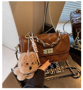 Detail of dark brown quilted crossbody bag with gold twist lock and plush puppy charm