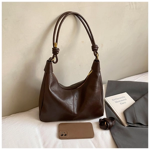 Detail view of dark brown Hobo shoulder bag with knot straps and a smartphone for size