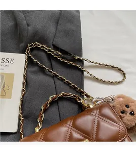 Detail view of brown quilted leather crossbody bag with gold chain and plush bear charm
