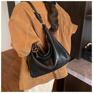 Detail of minimalist black oversized hobo bag with knotted strap and circular charm
