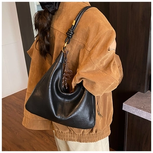 Detail of black pebbled leather hobo bag with knotted shoulder strap and round logo charm