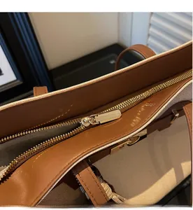 Close-up of the smooth golden metal zipper detail on a brown leather and canvas tote bag