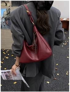 Detail of burgundy hobo bag with thick knotted shoulder strap and round metallic charm