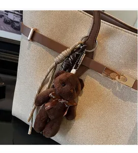 Close-up of a brown plush bear charm with Love bow tied to a beige tote handbag