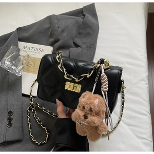 Detail of black quilted chain bag with gold twist lock and cute teddy bear charm