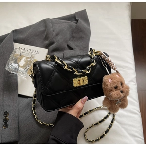 Detail of black quilted leather crossbody bag with gold lock and cute dog plush charm