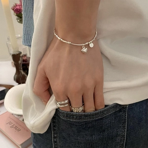 Dettaglio del bracciale a cuore in argento S925 e anelli geometrici su abbigliamento denim