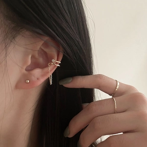 Nahaufnahme einer goldenen Doppel-Ohrklemme mit Kette und minimalistischen Ring-Sets