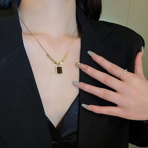 Ensemble collier et bague dorés avec pendentif carré noir porté par un mannequin