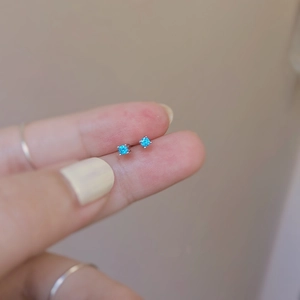 Macro view of mini S925 silver stud earrings featuring blue zircon in a four-prong setting