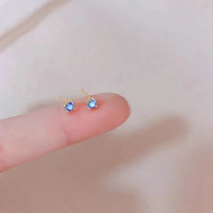 Macro shot of mini blue zircon earrings with gold prongs held by hand for size