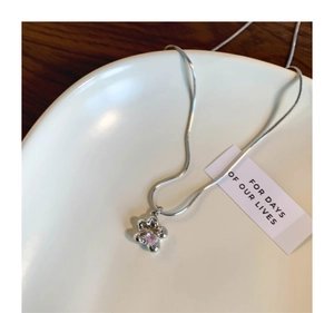 Détail d'un collier chaîne serpent argentée avec pendentif fleur en zircon rose sur plateau