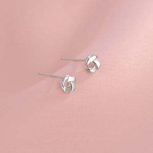 Minimalist S925 sterling silver knot stud earrings with polished finish on pink silk
